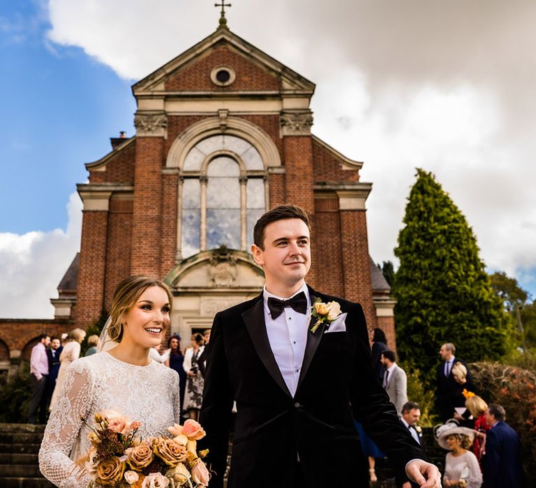 Bride with updo and fitted wedding dress with groom in black tie exit their wedding ceremony 