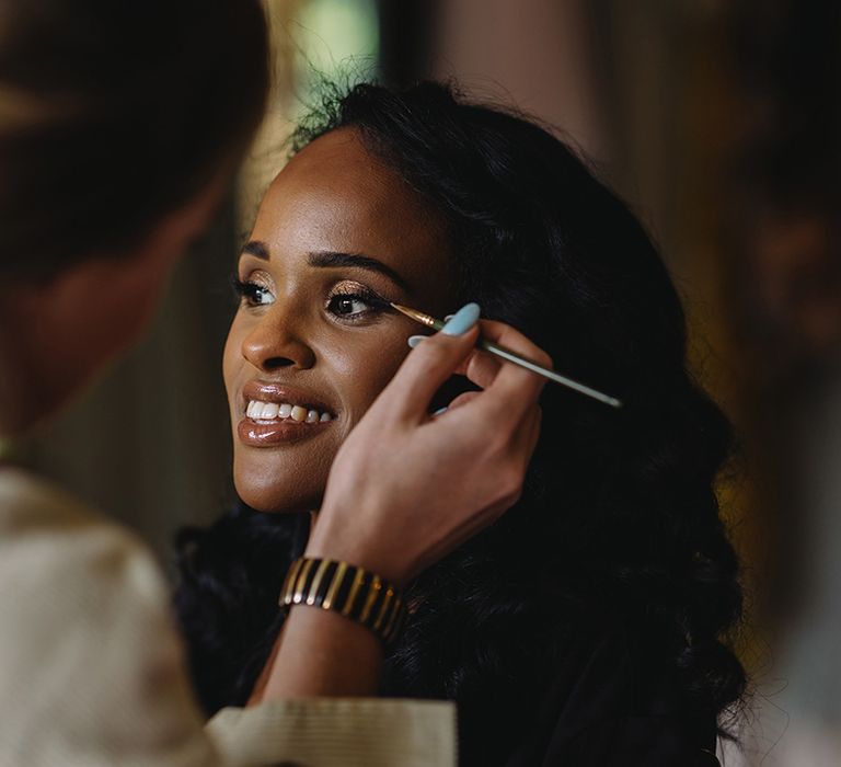 Bride gets her makeup done for her wedding with gold smoky eye and lipgloss