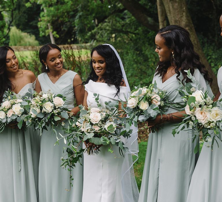 Bride with bridesmaids in mint green various style dresses all holding white rose bouquets with eucalyptus leaves