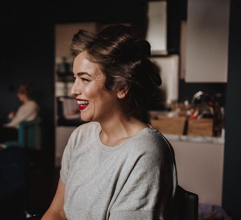 Bride has her hair pin curled smiling wearing red lipstick for her wedding day as she gets ready 