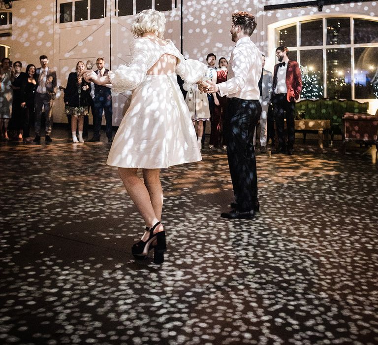 Bride in short wedding dress with groom in shirt and suit trousers have their first dance 