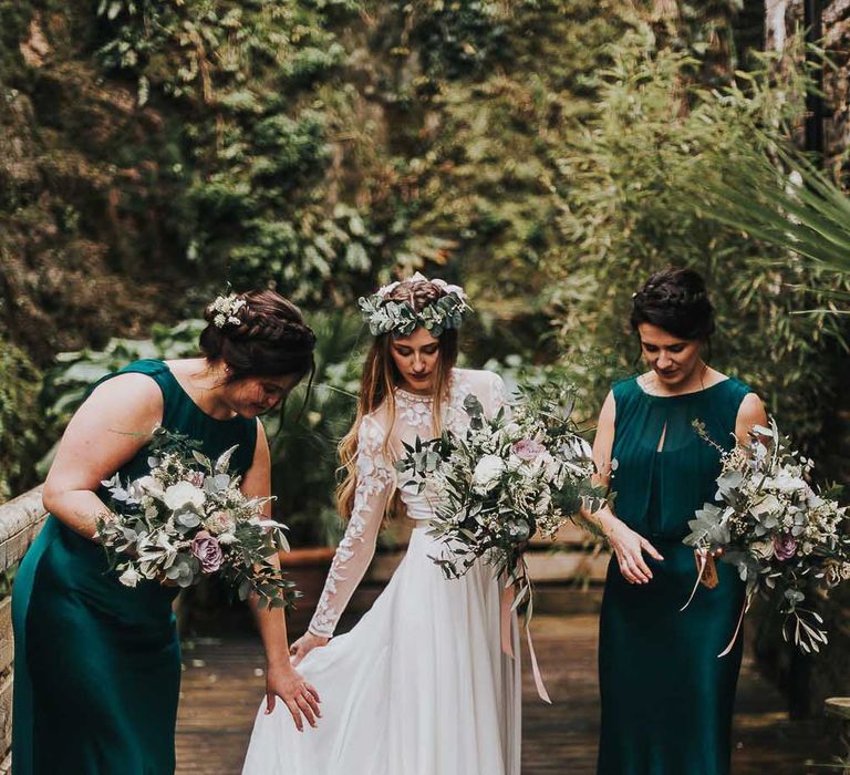 Bridesmaids in forest green dresses with braided hairstyle helps the bride in a lace wedding dress 