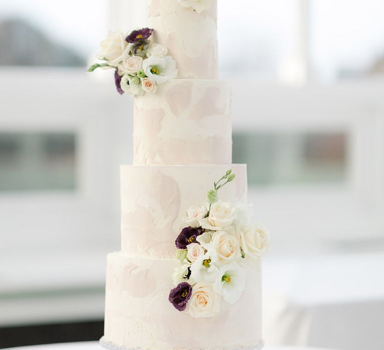 Four tier wedding cake finished with pale pink and white frosting complete with floral decoration 