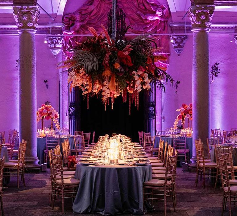 Pink lit wedding venue for reception complete with extravagant floral installation above table 