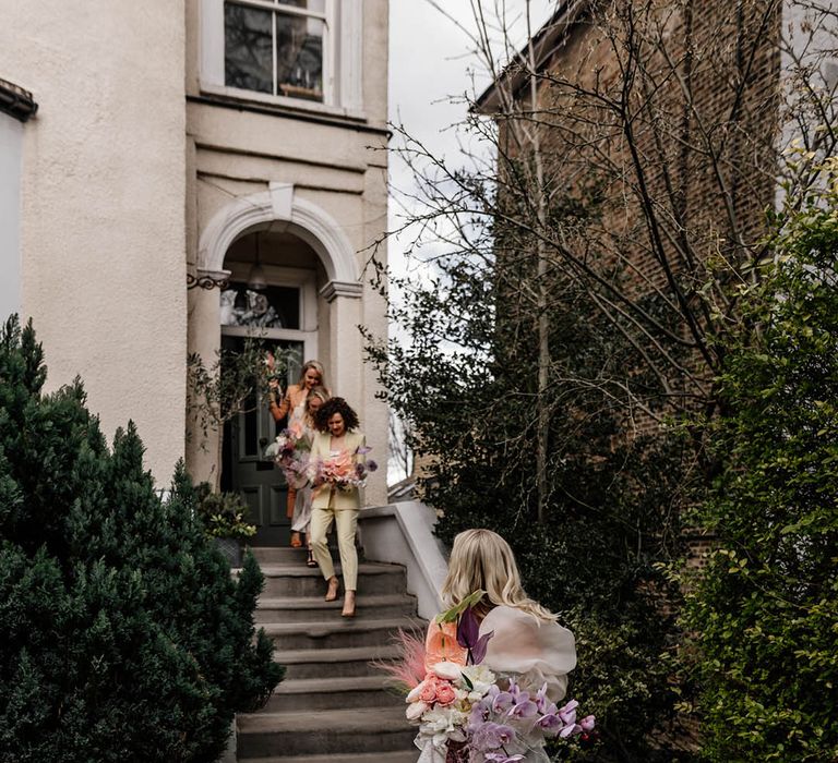 bridal party in colourful bridesmaid suits walking down steps to meet the bride in a Jesus Peiro wedding dress