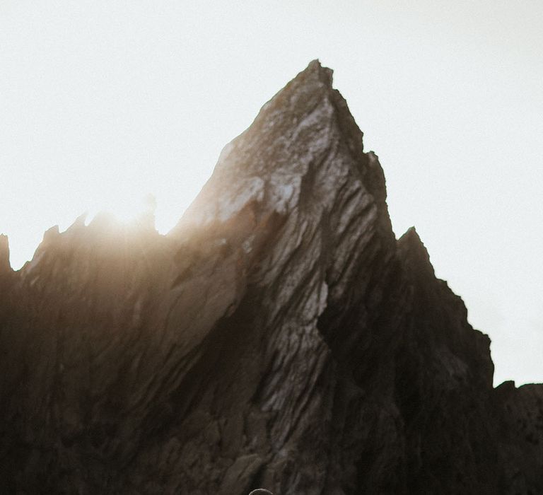 Sun shines across rocks as bride & groom kiss outdoors during couples portraits on the rocks 