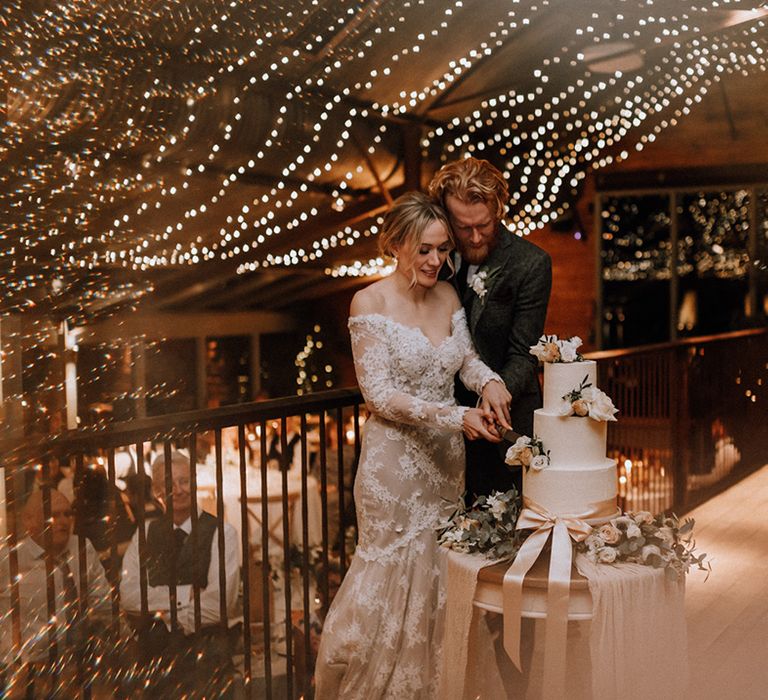 Bride and groom cut their wedding cake surrounded by fairy lights