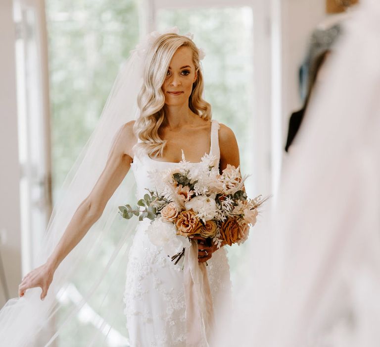 Bride getting ready for her wedding day in a 3d floral applique wedding dress holding rustic bouquet 