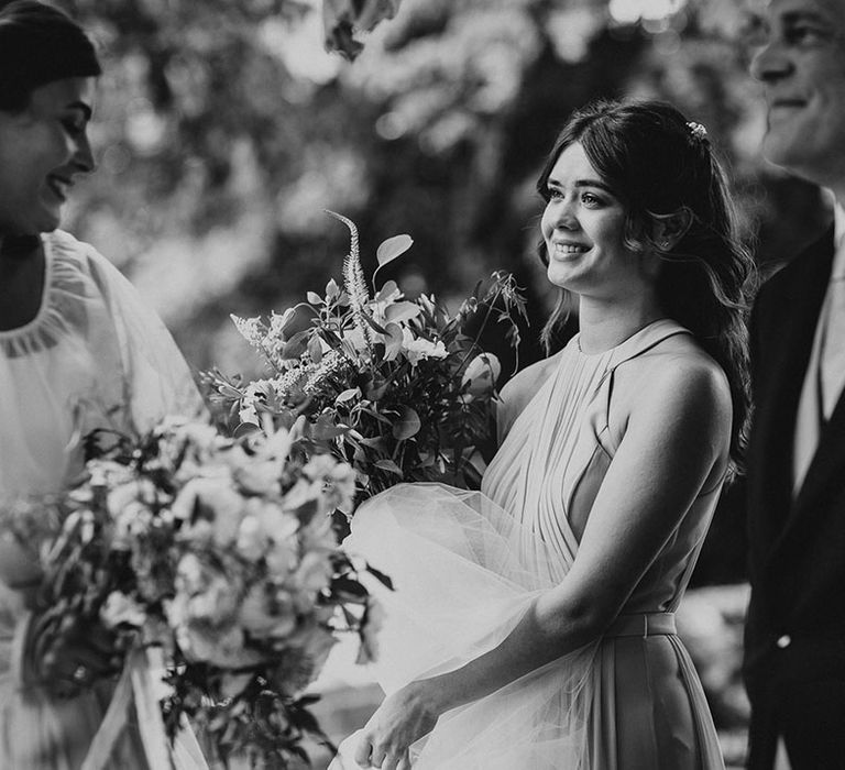 Bridesmaid stands smiling holding the bride's train and veil out of the way 