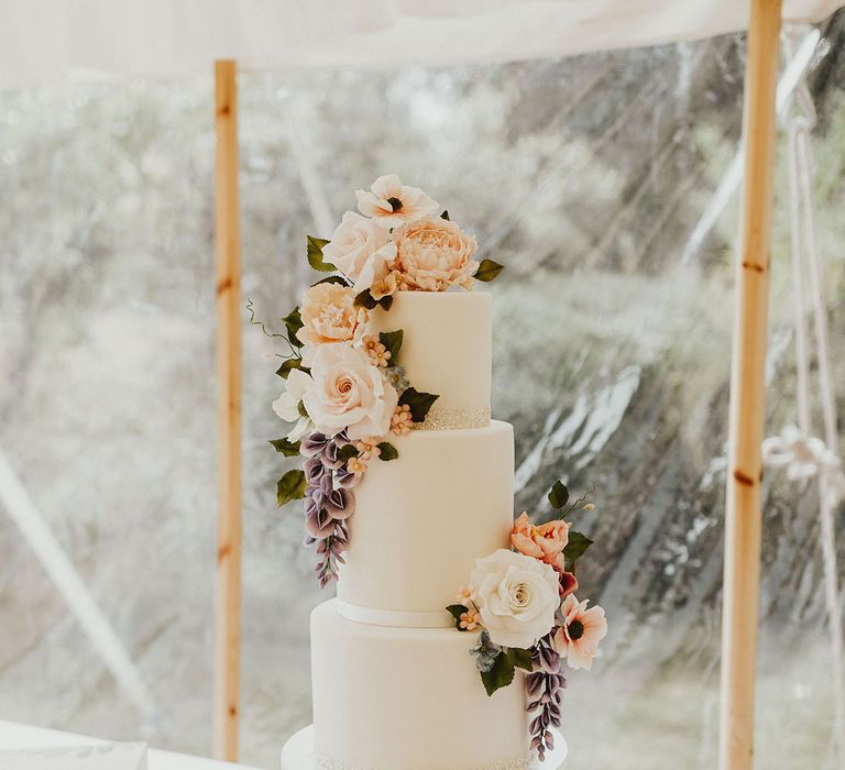 Three tier white iced wedding cake with ribbon and glitter borders decorated with pink and purple flowers 