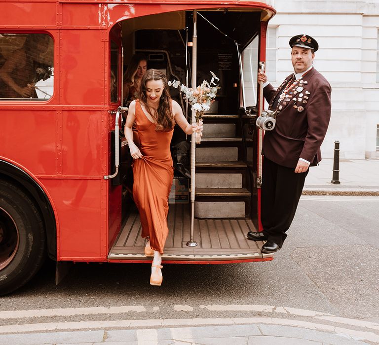 Bridesmaid wears fitted burnt orange bridesmaid dress whilst holding dried floral bouquet 