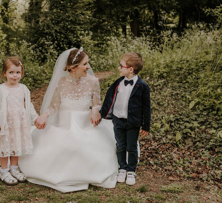 Bride in a high neck sheer long sleeve Suzanne Neville A-line wedding dress with two young children 