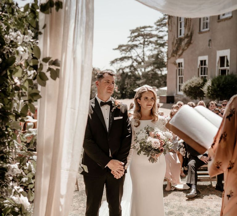 Groom in black tie with the bride in a Badgley Mischka wedding dress with drapery and blush pink flowers 