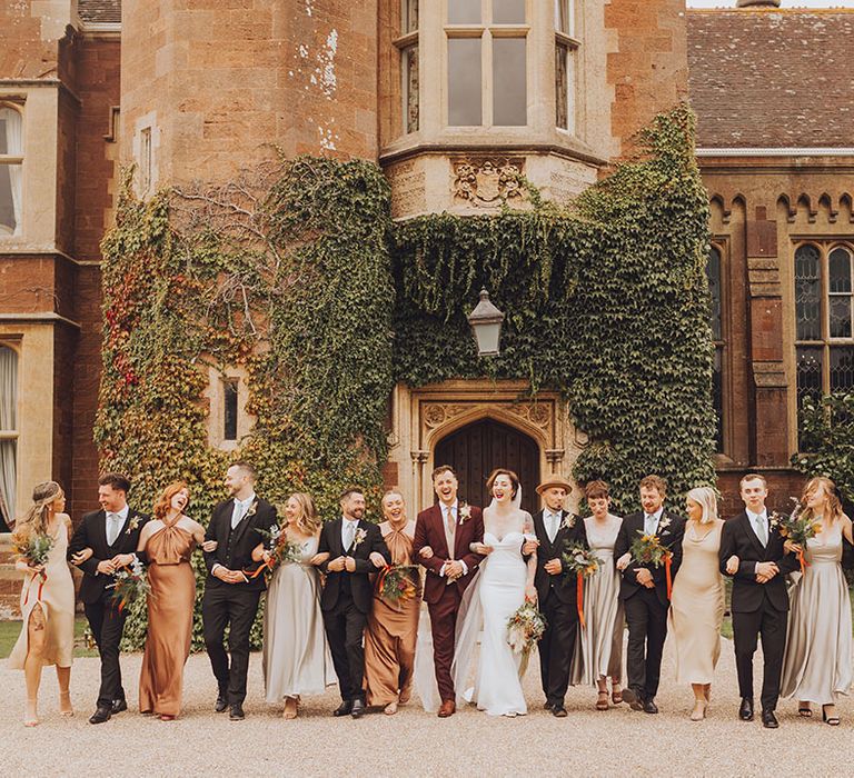 Bride & groom walk with wedding party who wear mismatched bridesmaid dresses in Autumnal colours 