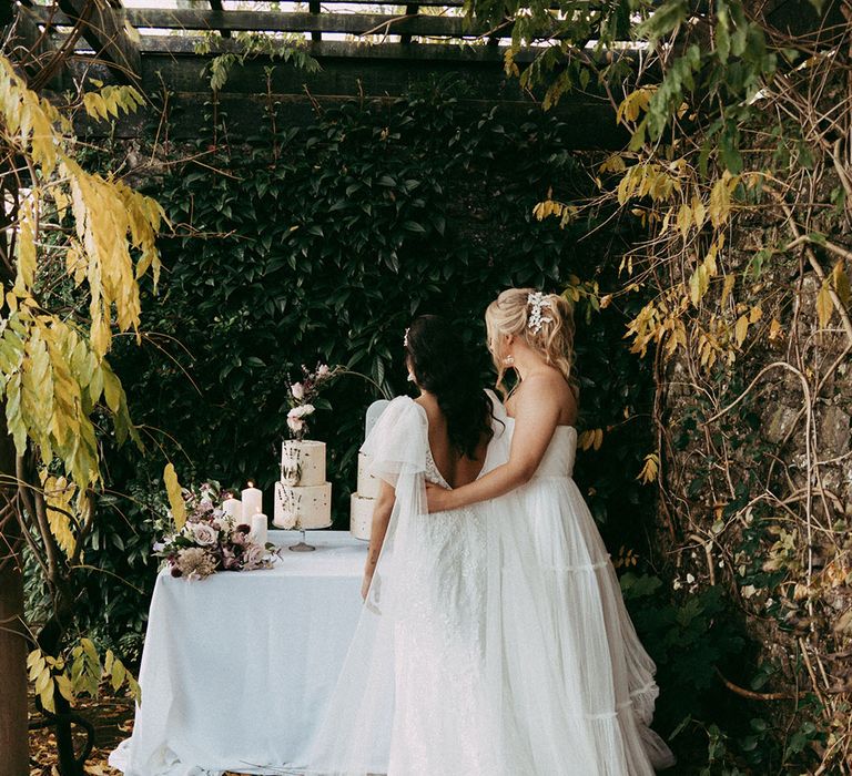 Bride in open back detail lace wedding dress with short puff lace sleeves and bride in sleeveless layered tulle wedding dress at the alter at Holesfoot venue