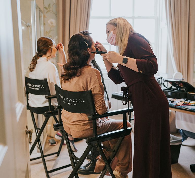 Bridesmaids sit on black chairs as they get their makeup done for the gay wedding 