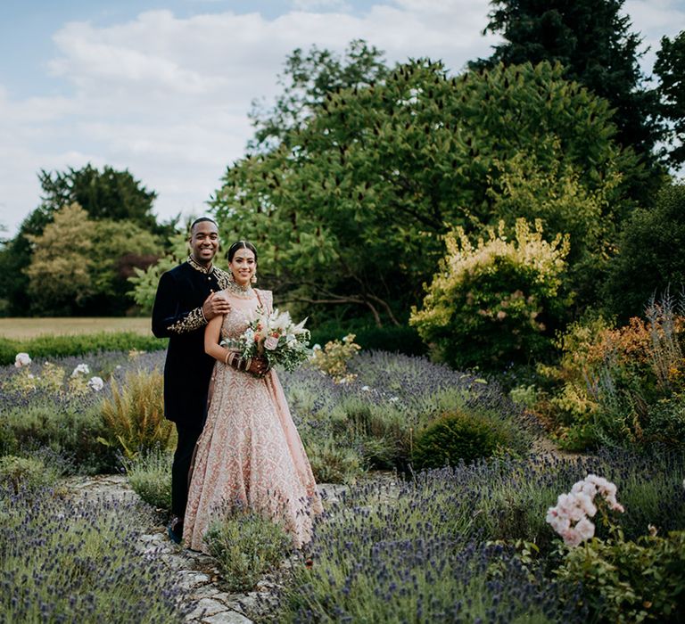 Bride and Groom pose in the grounds of Caswell House surrounded by lavender 