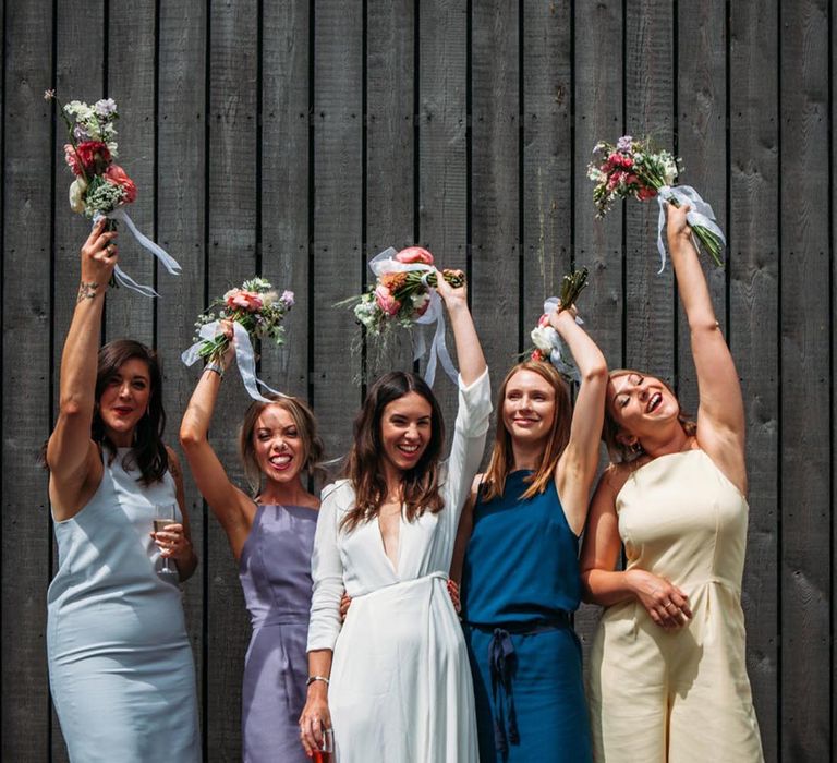 Different colour bridesmaid dresses for the bridal party lifting their bouquets with the bride 