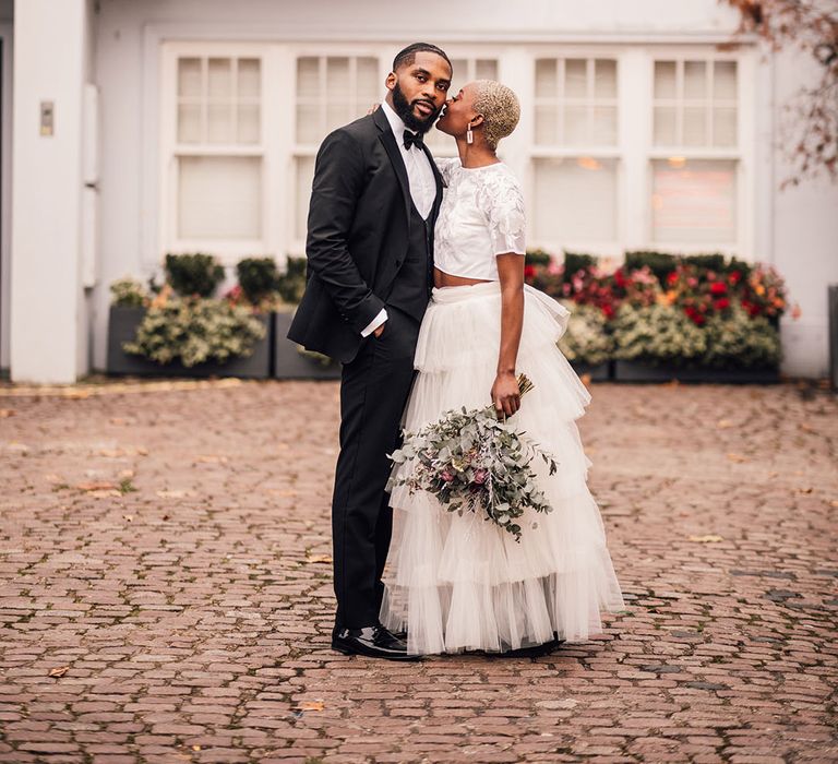 London Bride kisses Groom whilst holding a bridal bouquet featuring pink roses, eucalyptus and waxflowers