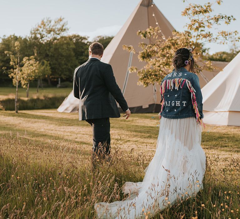 Bride in colourful personalised denim jacket walks with her groom