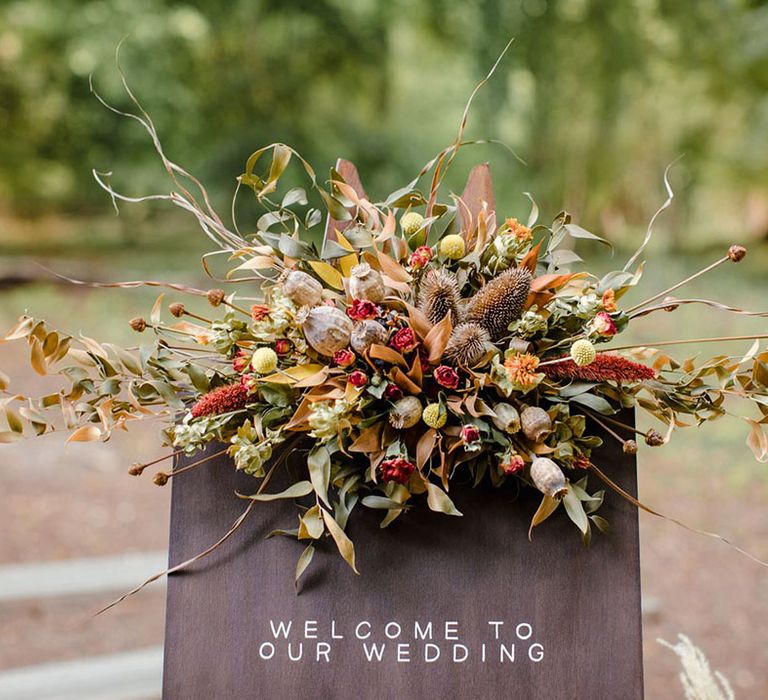 Large autumnal bouquet with dried flowers, pampas grass, red roses and foliage on top of a wedding welcome sign