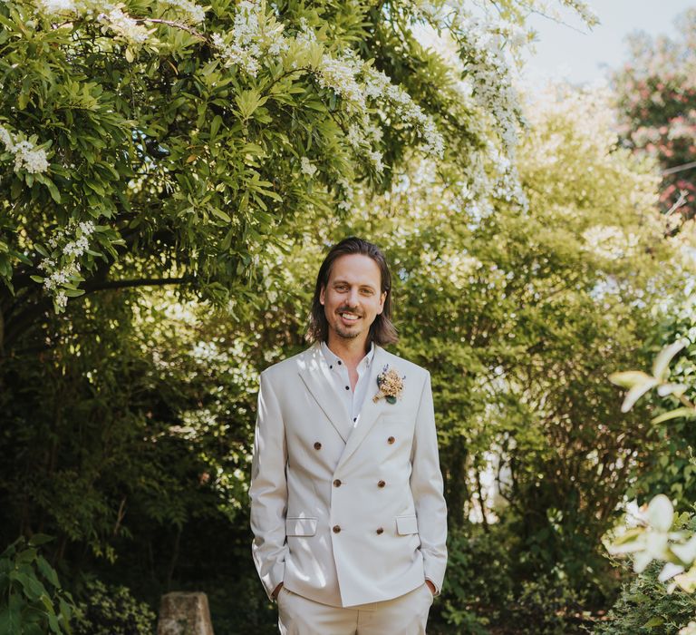 Groom posing in garden of The Reid Rooms venue wearing neutral coloured double-breasted ASOS suit and black high-top converse with dried flower and foliage boutonniere 