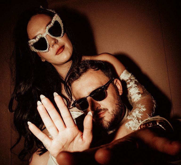 Bride in bejewelled cat eye sunglasses and groom in classic Raybans sunglasses posing at fun, relaxed wedding