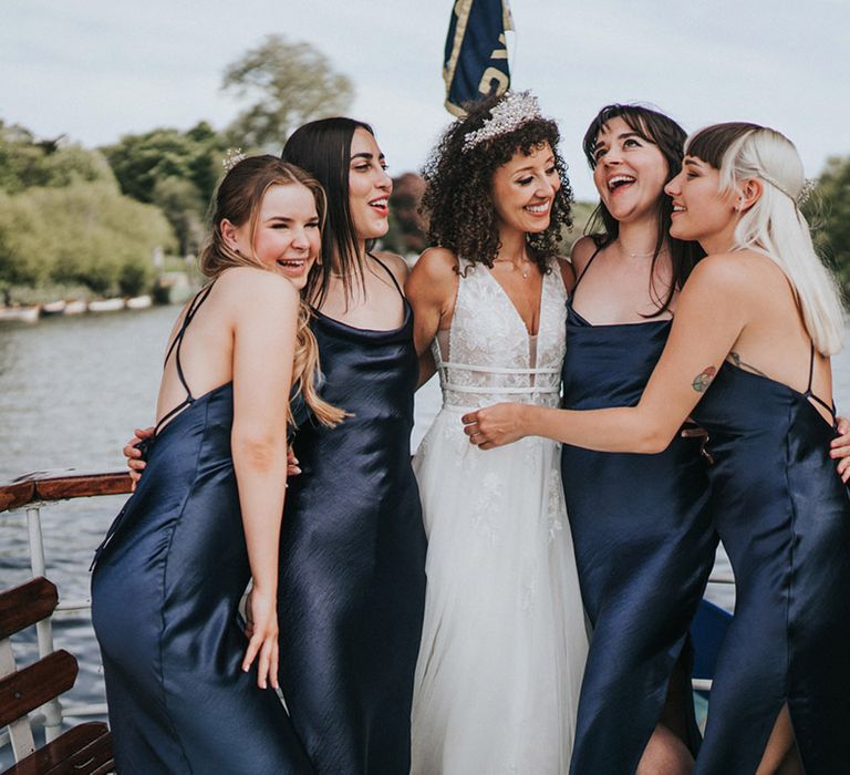 Bride stands alongside her bridesmaids in navy midi bridesmaid dresses during Thames boat ride 