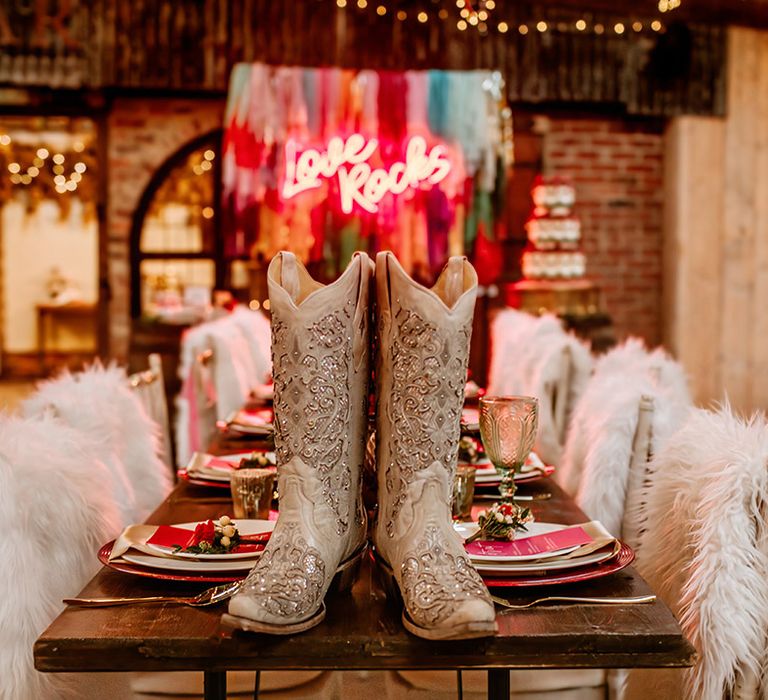 Bridal cowboy boots with silver sparkly details on rustic retro wedding tablescape with streamer decoration ideas and hot pink neon sign in the background 