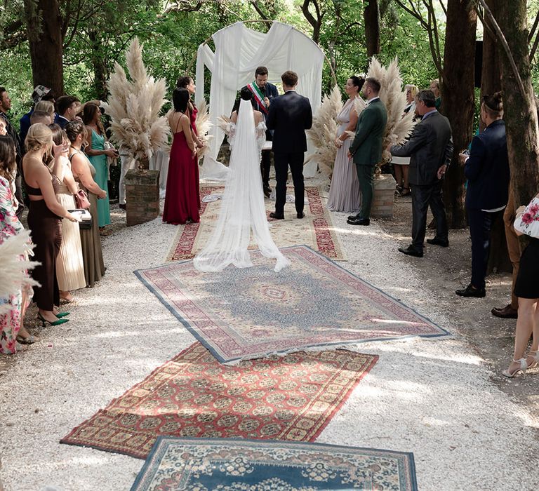 Moroccan styled rugs leading to draped archway complete with pampas grass installations for boho destination wedding 