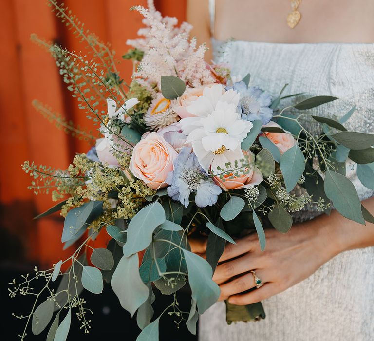 Bride holds homemade bridal bouquet complete with seasonal pastel coloured blooms