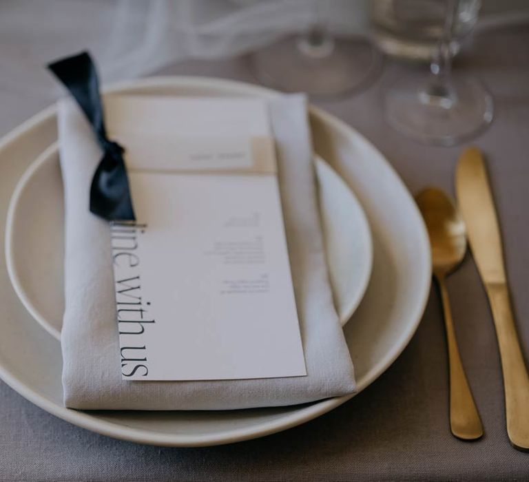 Minimalistic wedding menu with black ribbon and elegant lettering on luxury ceramic plates next to gold cutlery 