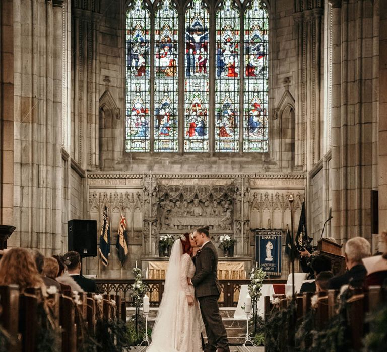 Traditional church wedding with small candles for the indoor aisle decoration with foliage tied onto the end of the pews 