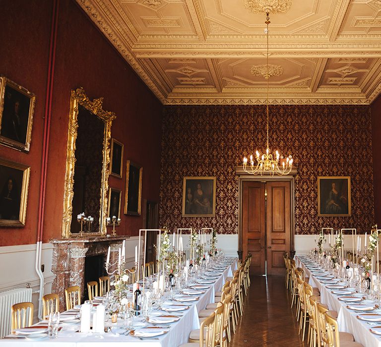 Classic wedding tablescape with white table cloth, tapered candles in gold candelabras, pillar candles, gold frame decorations, gold plates, gold cutlery and dried flower and white rose floral arrangements at Grittleton House 