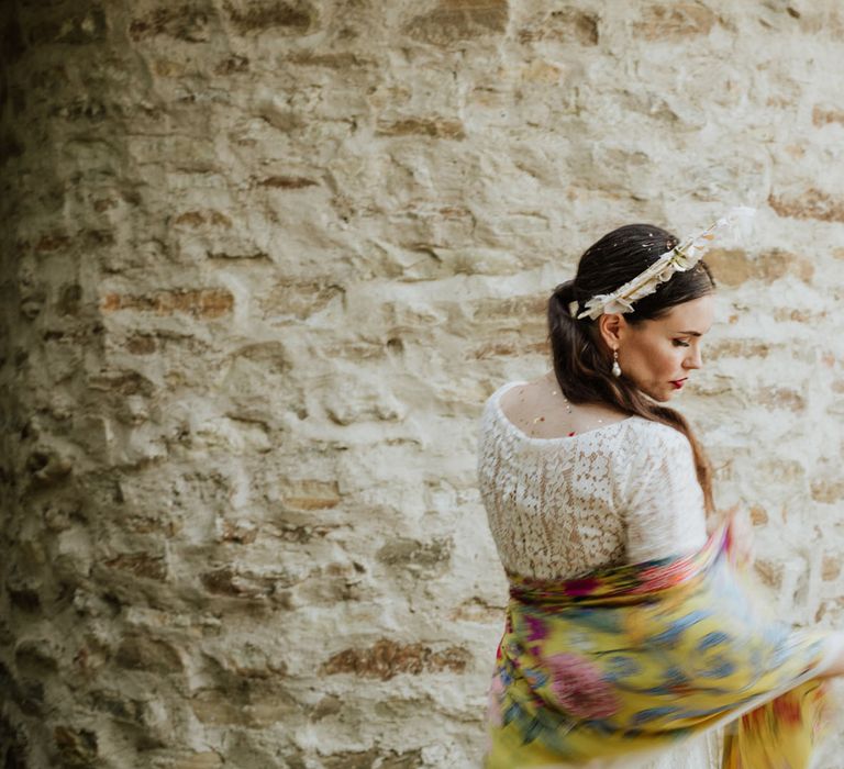 Bride at rustic wedding venue wearing white lace wedding dress, boho bridal crown and yellow floral pashmina