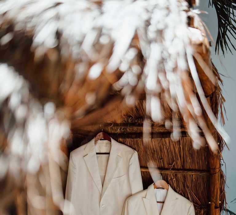 Mens white wedding suit on hangers at tropical destination beach wedding 