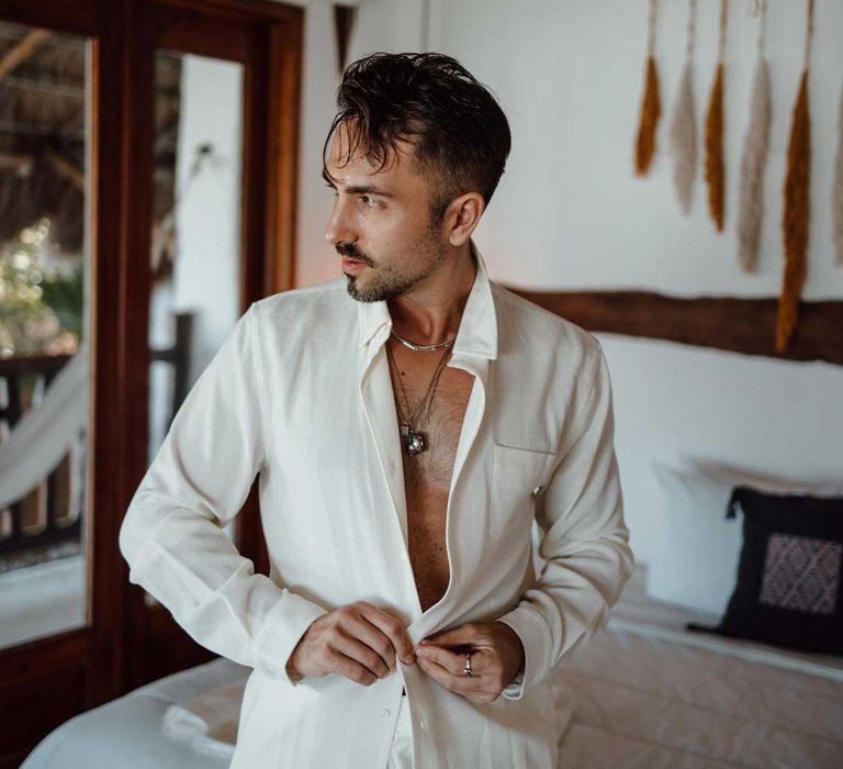 Groom putting on white linen grooms shirt at destination wedding 