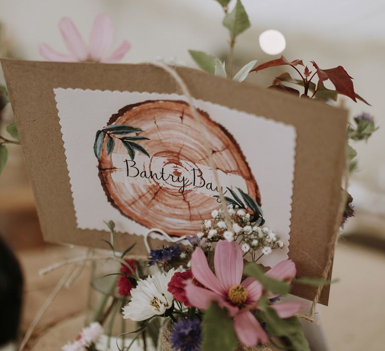 DIY cardboard wedding table name idea resting on wooden tree slice decorated with wildflowers and tea lights 