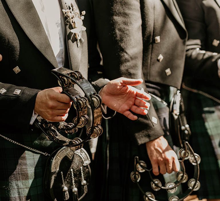 Groomsmen in green checkered kilts play tambourines at the wedding ceremony 