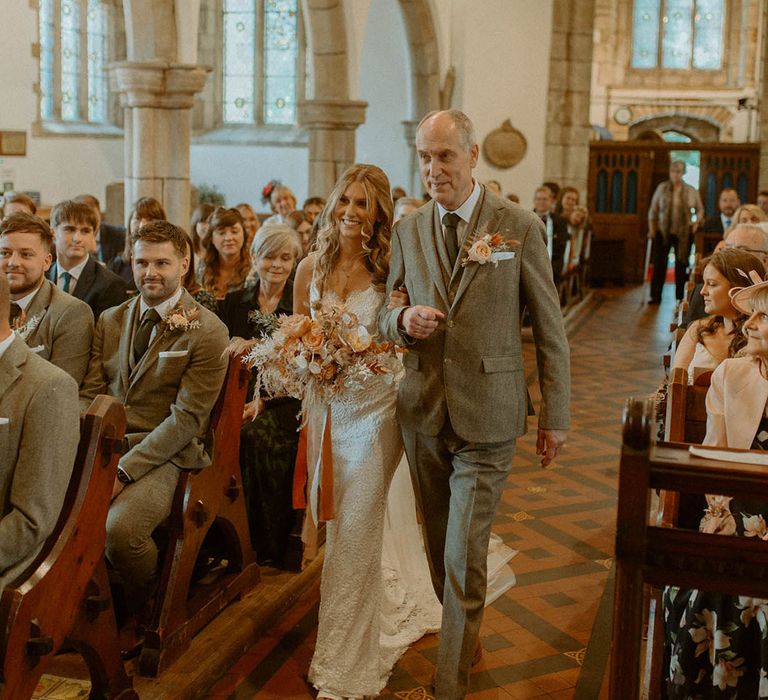 Groom in grey suit walking down the aisle with the bride in lace wedding dress at church wedding 