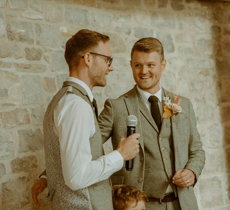 Groom stands up with the best man who reads out a best man speech for the wedding reception 