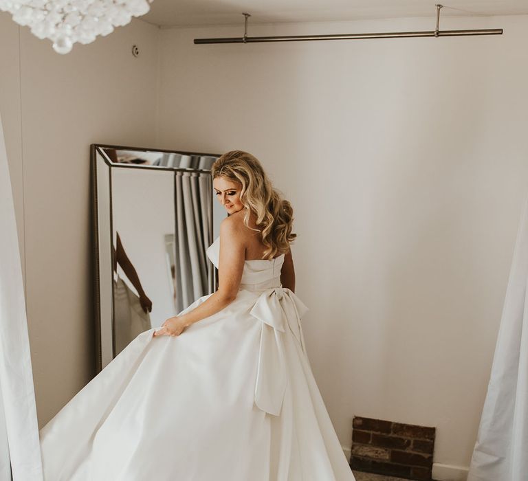 Bride with blonde bouncy curled wedding hair in strapless gown with large bow detail on the back of the dress 