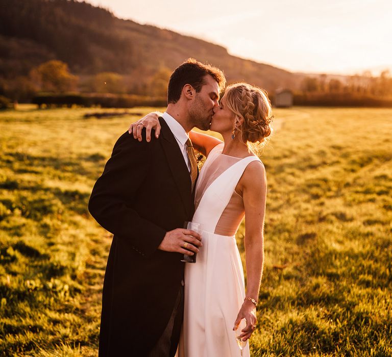 Bride with braided crown hairstyle on blonde hair kissing the groom during golden hour 