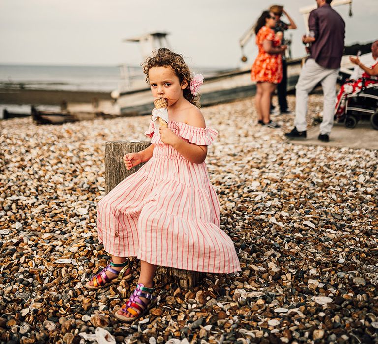 young wedding guest in a red and white stripy dress eating ice-cream on Whitstable beach at East Quay wedding 