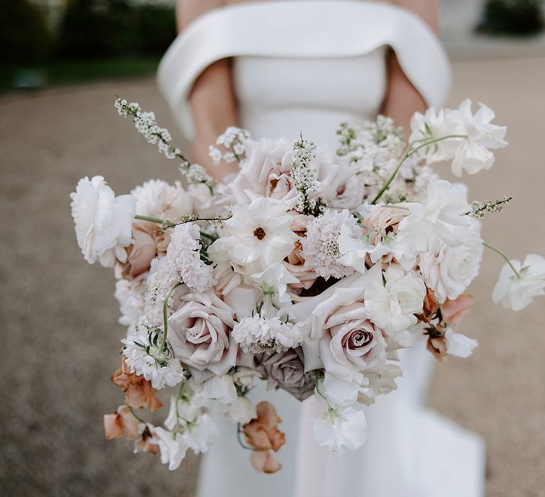 Pale pink and white wedding bouquet held by bride in off the shoulder wedding dress