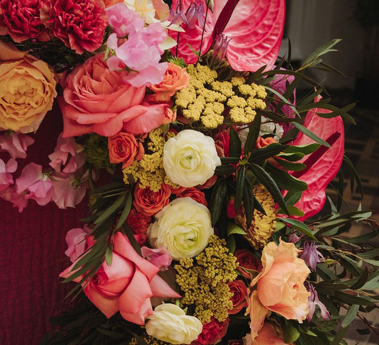 Roses, anthuriums, orchid, peonies and more in pink, orange, and yellow wedding flower arrangement 