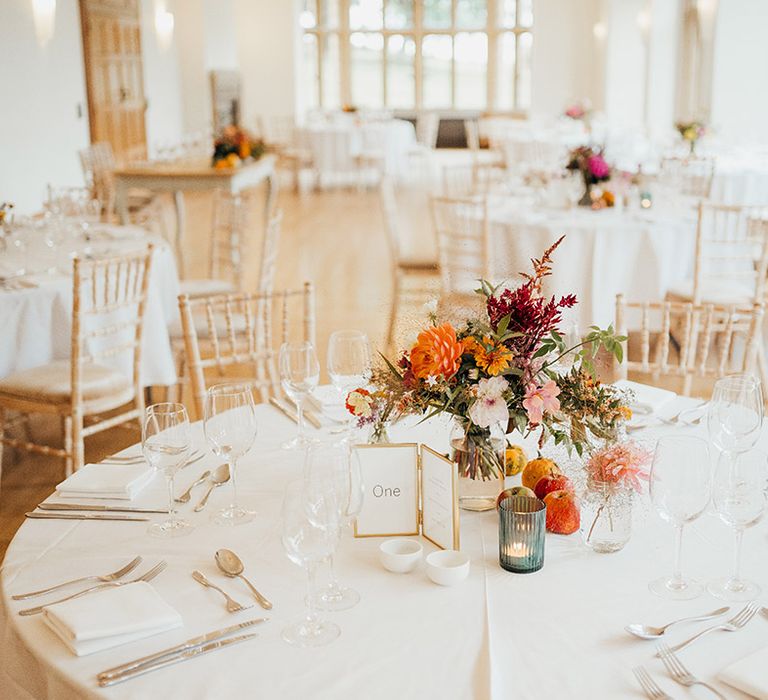 Autumnal table centrepiece with gold framed table number sign on white tablecloth with white napkins 