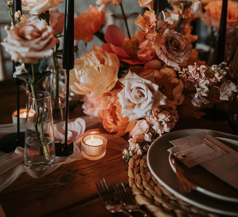 Black accent taper candles amongst pink and blush neutral wedding flower arrangements with tea lights 