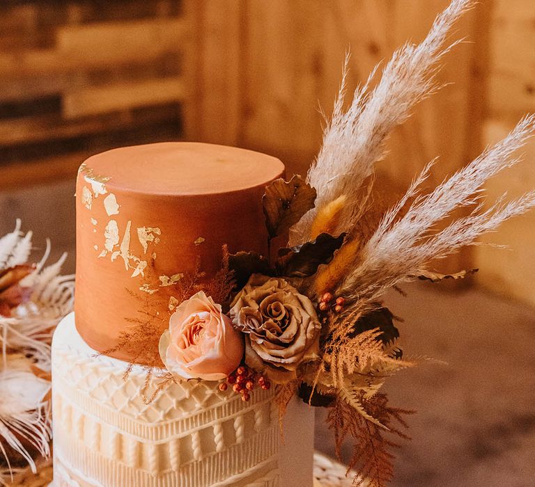 Two tier orange iced wedding cake with boho macrame style decoration and pampas grass 