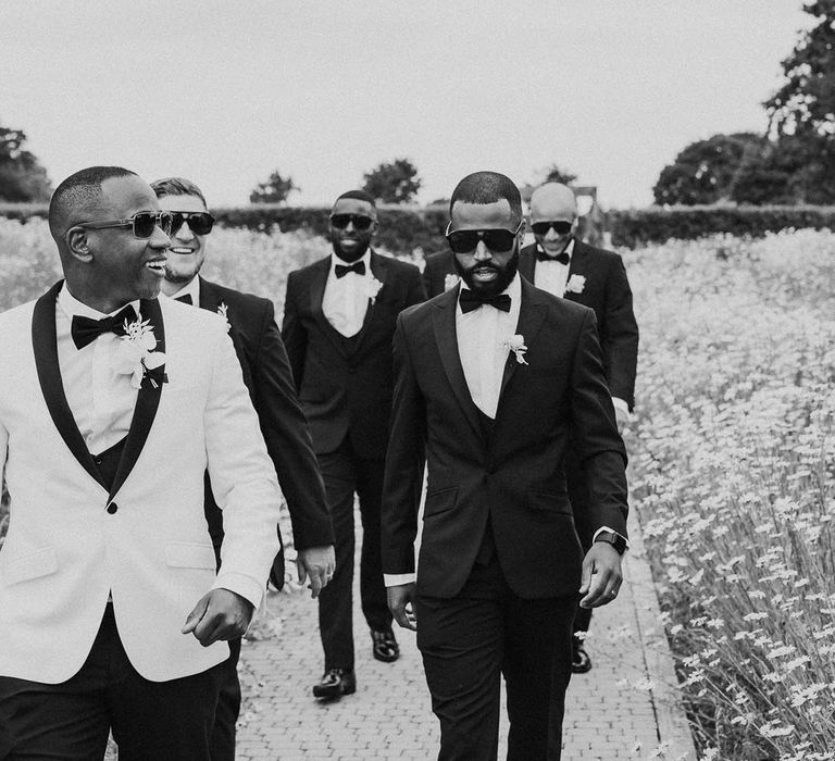 Groomsmen in-black tuxedos and sunglasses walks with groom in black and white tuxedo at Crumplebury wedding